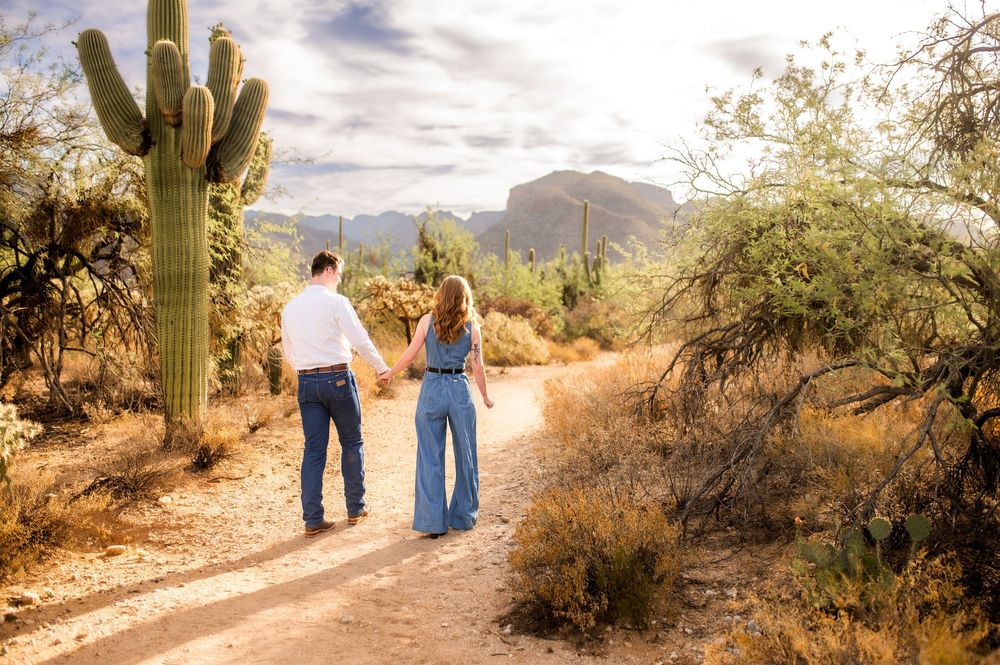 Couple walks hand in hand down a desert path with saguaro cactus and Superstition Mountains at golden hour.