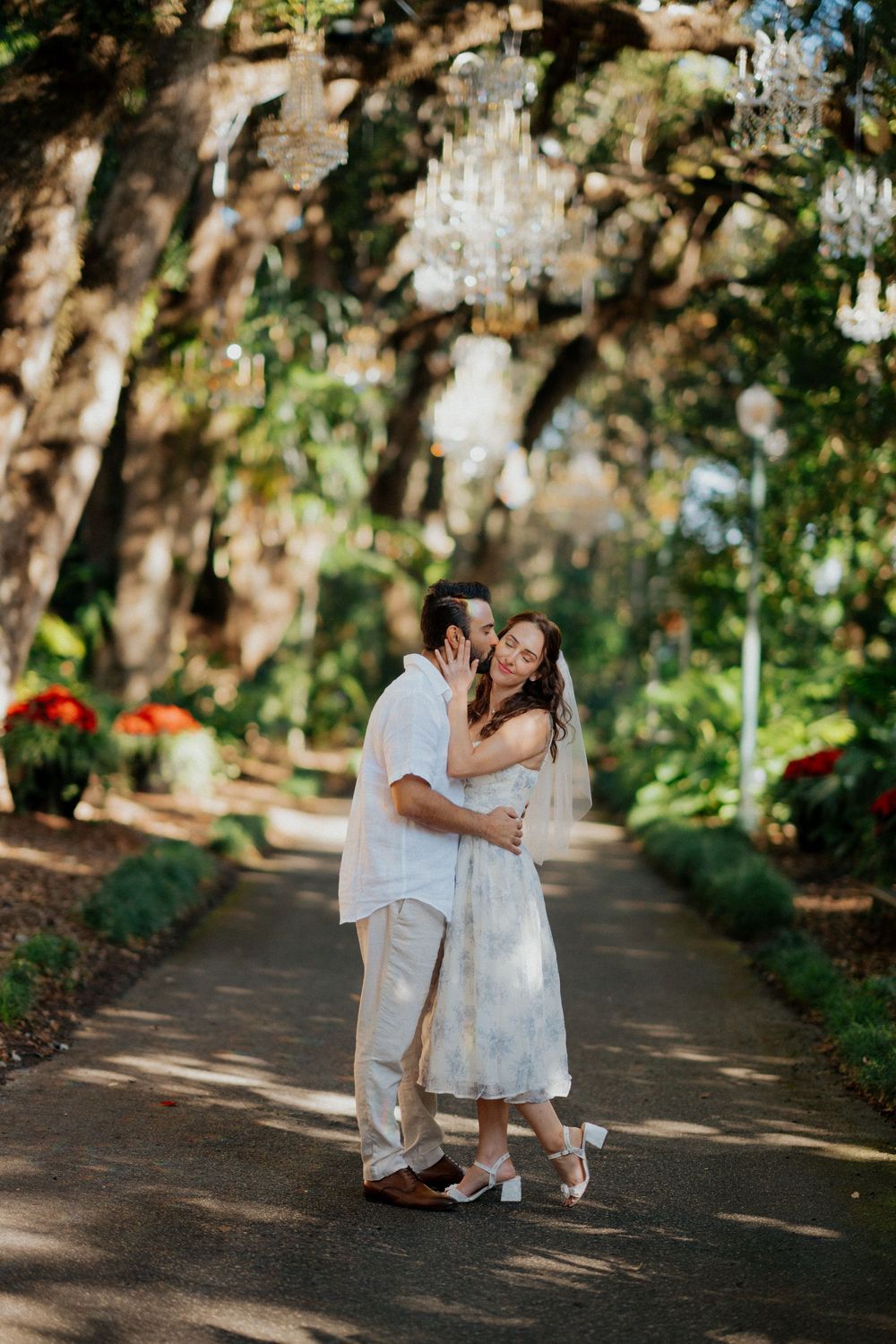 A couple shares intimate moments along a tree-lined path with Spanish moss hanging overhead.