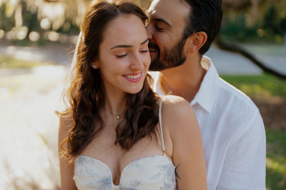 Romantic couple in wedding attire share intimate moments during outdoor photo session in natural sunlight.