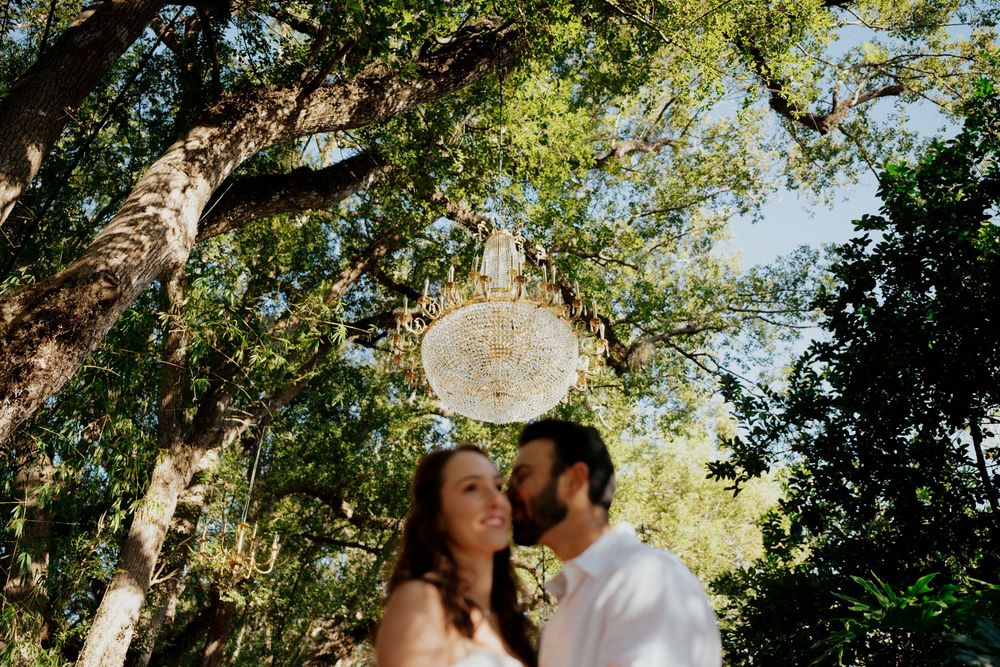 Couple shares a romantic moment in a lush garden setting under sunlit trees at Harry P Leu Gardens