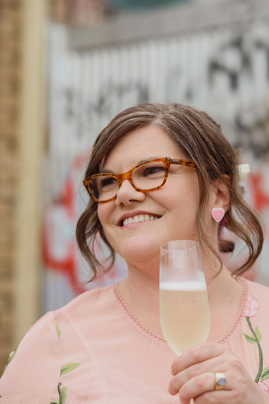 Person wearing glasses and pink clothing smiles joyfully while holding a beverage glass.
