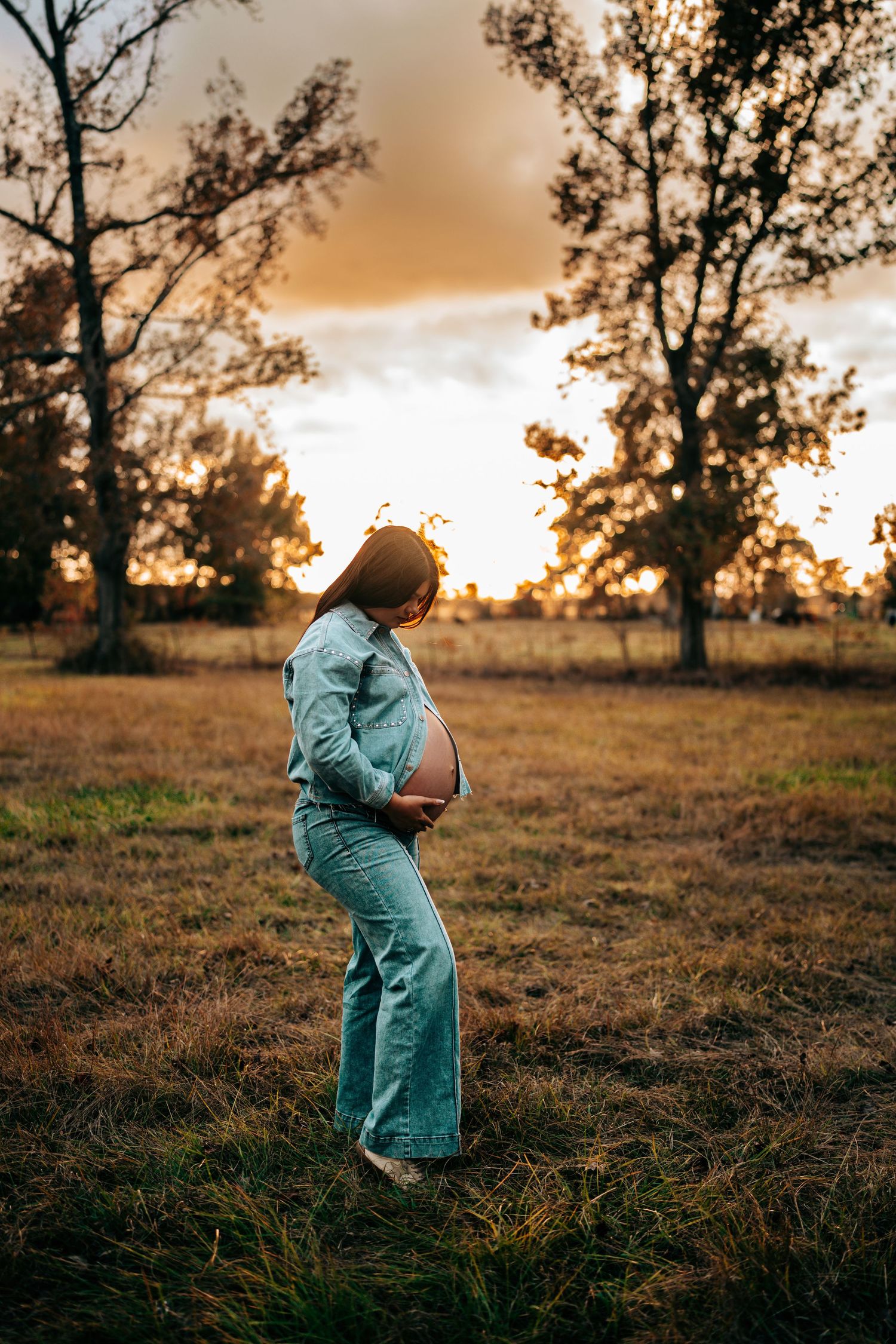 Person in teal dress twirls in a golden field at sunset with trees silhouetted in the background.