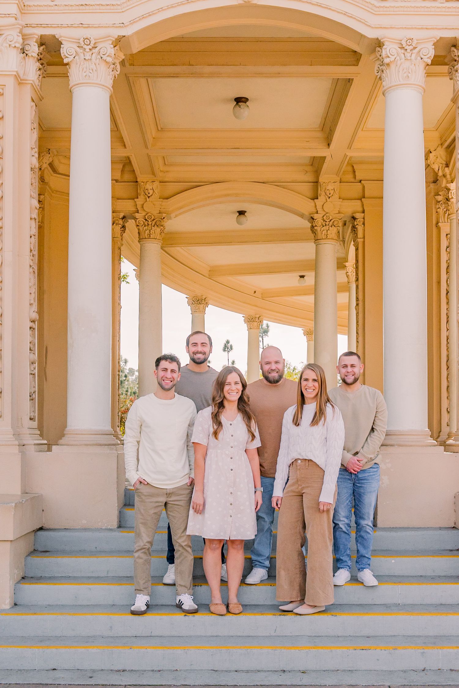 Group portrait taken in front of a classical colonnade with ornate pillars and archways in warm beige tones.