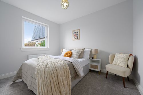 Modern bedroom interior with gray walls, white bedding, and natural light streaming through small window.