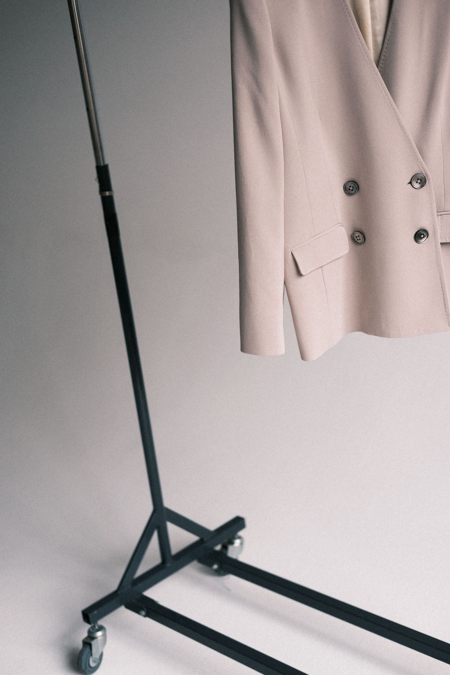 A minimalist clothing rack displays a light beige blazer against a white wall in a clean, modern setting.