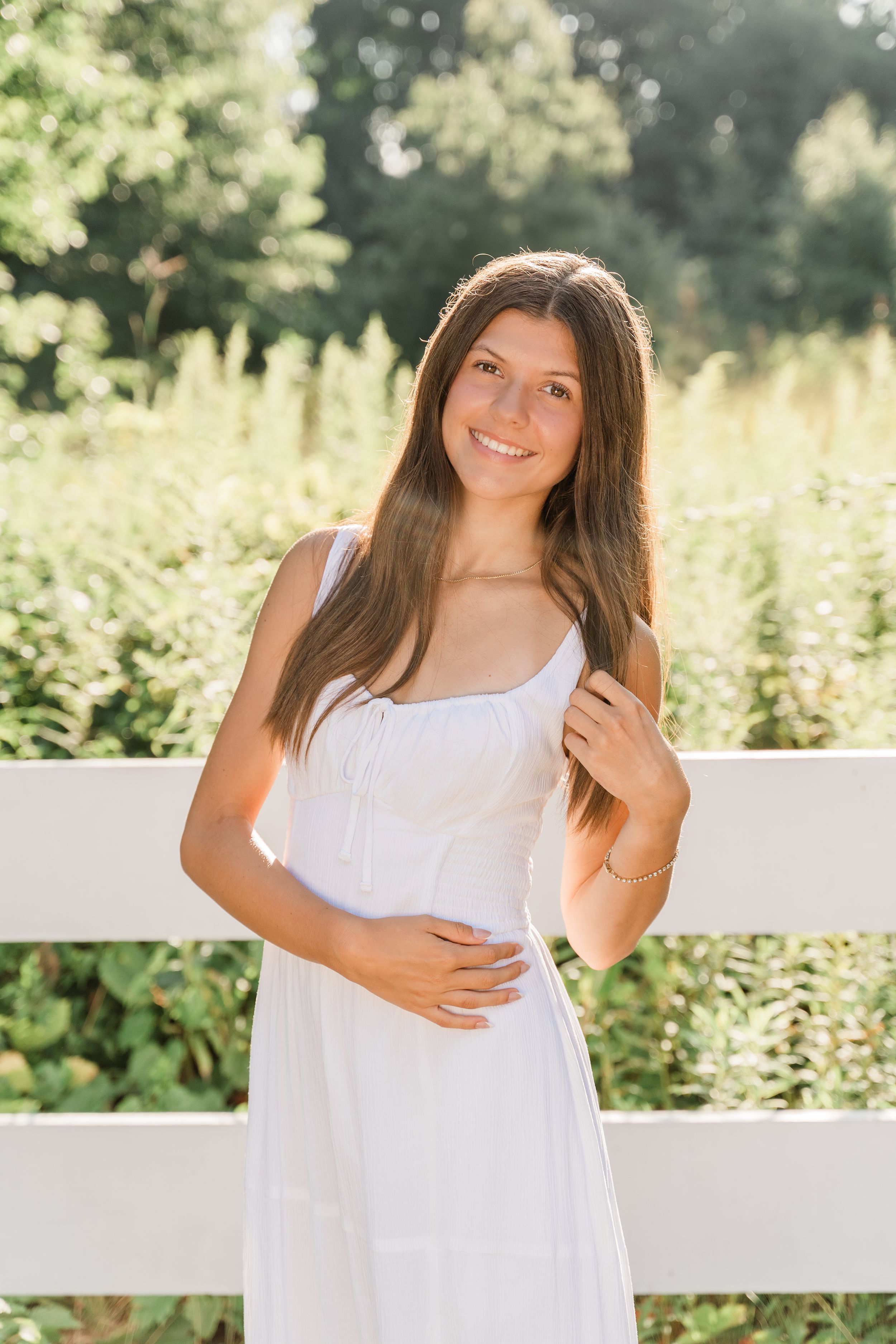 A summer portrait in a white dress against a rustic white fence and garden backdrop.