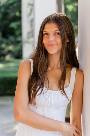 Portrait of someone wearing a white sleeveless dress against a bright outdoor background.