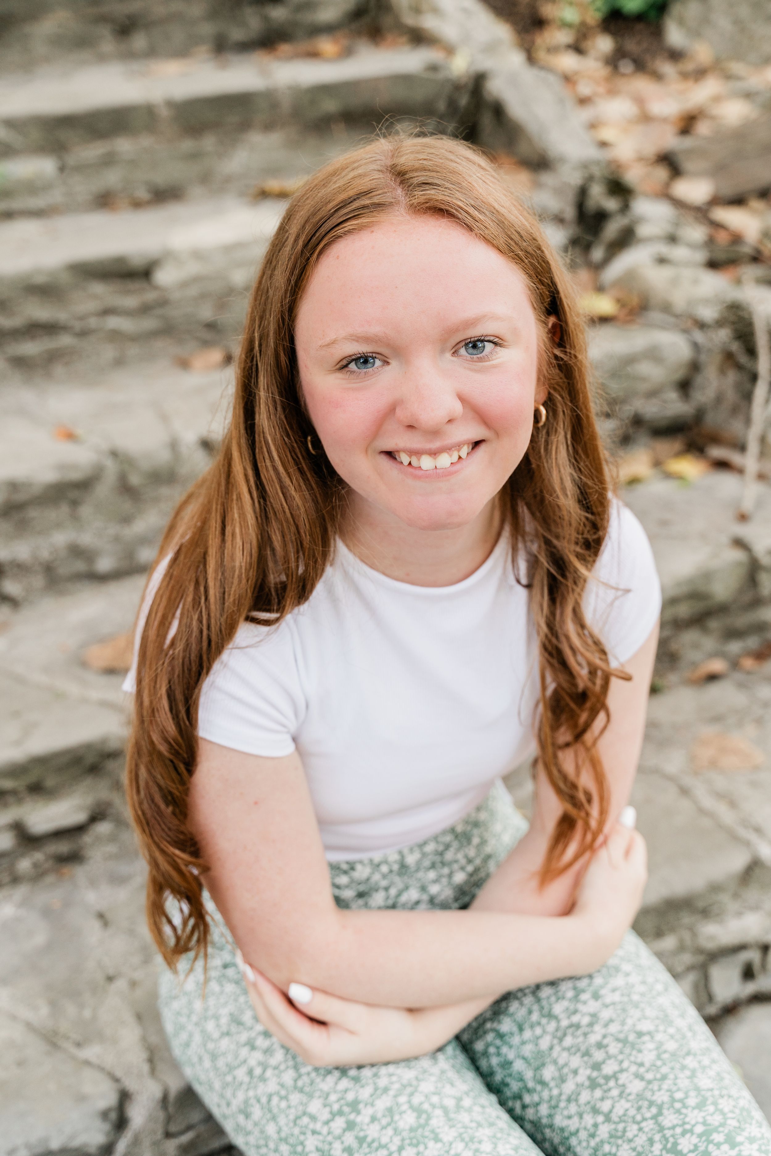 A person in a white t-shirt and floral skirt sits on stone steps during an outdoor portrait session.