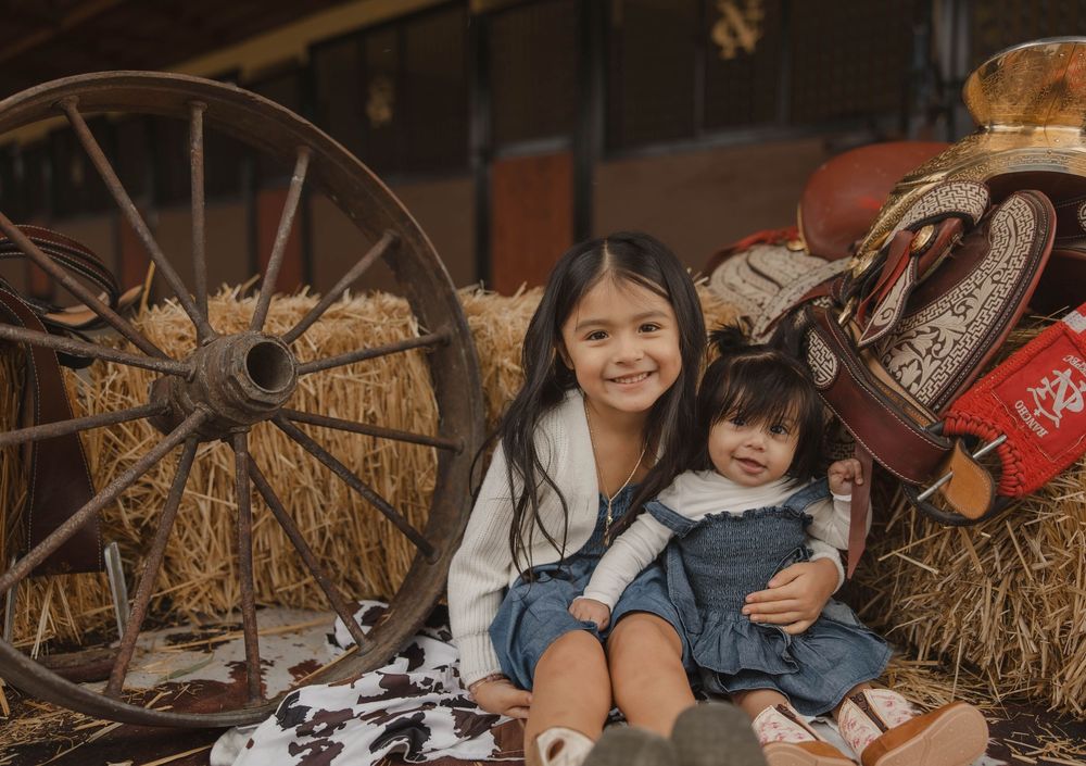 Western themed photo setup with hay bales and saddle decorations in a barn.