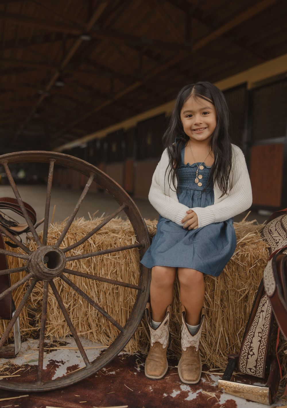Cowboy boots and denim outfit against rustic barn backdrop with hay bales.
