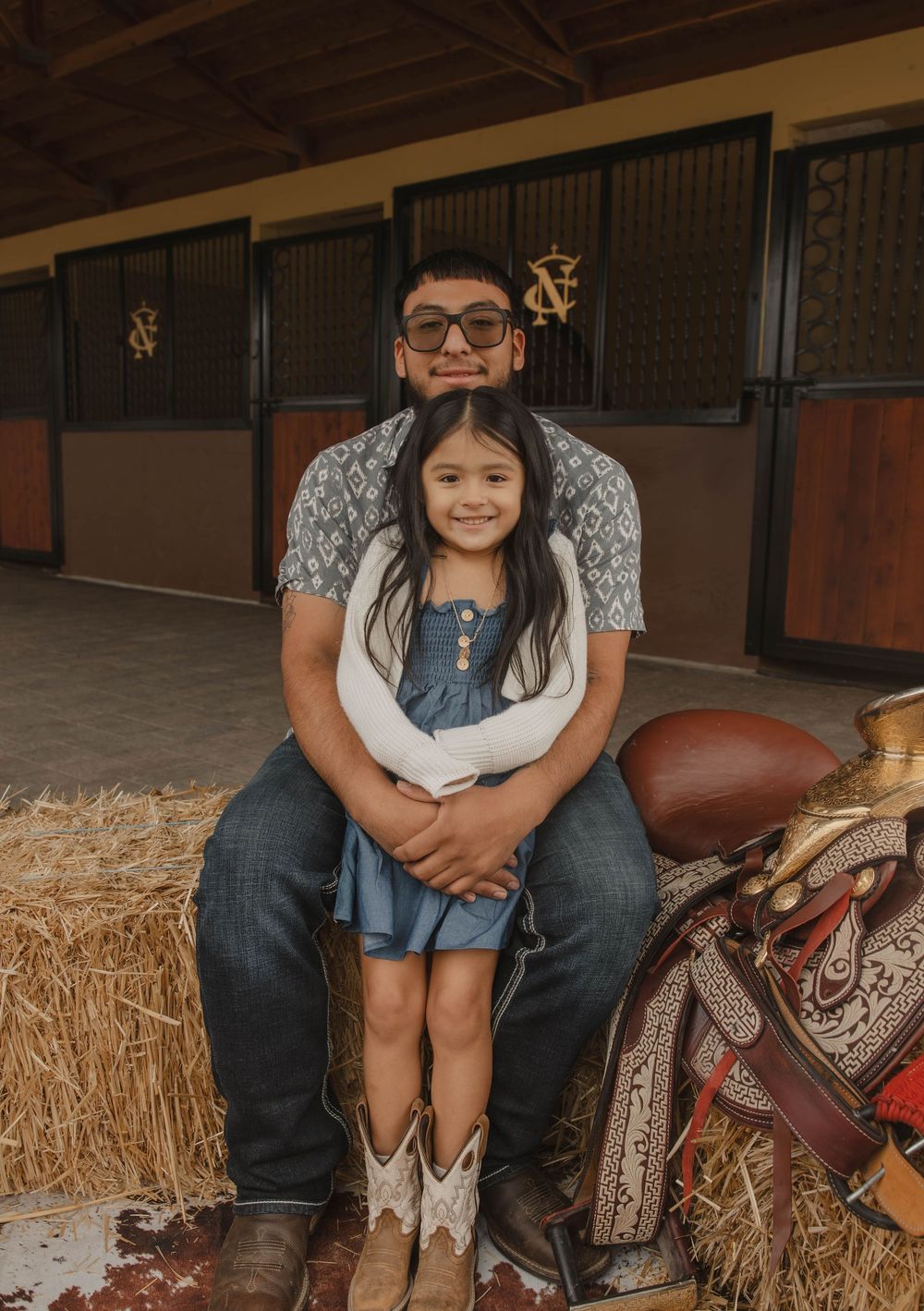 Casual portrait session in rustic barn with western props and hay bale seating.