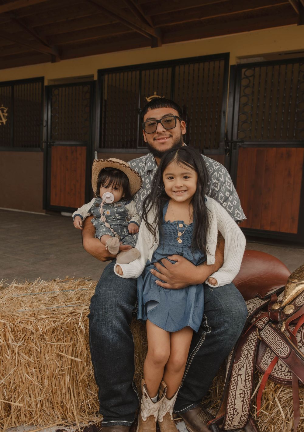 Family photo session in western-themed barn setting with hay bales and saddle decor.