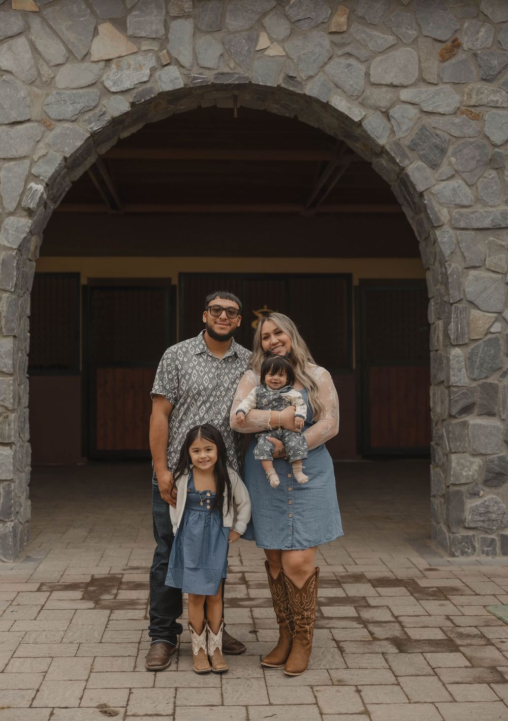 Family group poses casually under stone archways wearing coordinated western outfits.