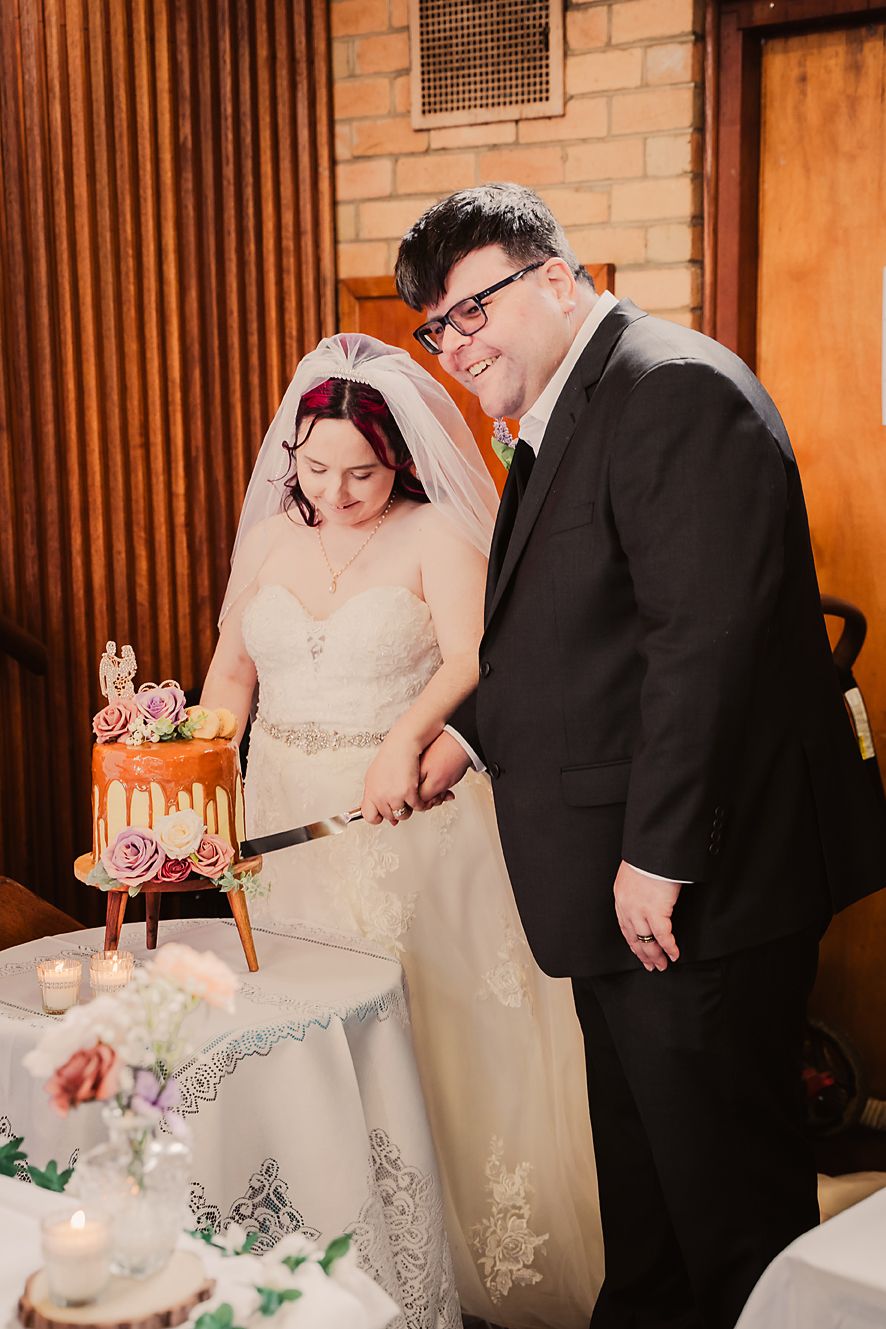A bride and groom share a joyful moment while cutting their wedding cake decorated with pink roses.