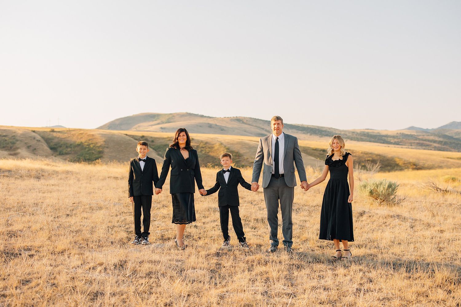 A group of people in black attire walking together across a golden autumn hillside at sunset.