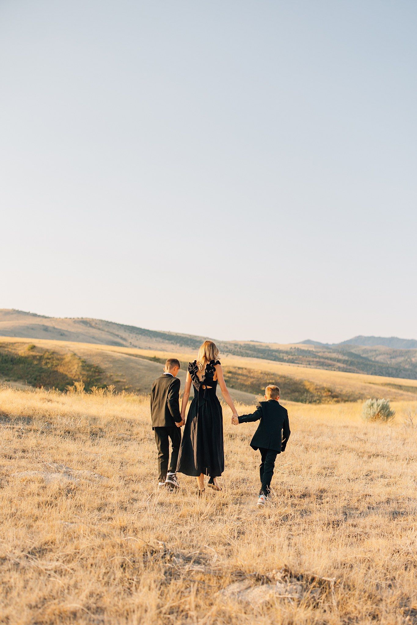 Group of people walking together across a golden grassy hillside during sunset with mountains in the distance.