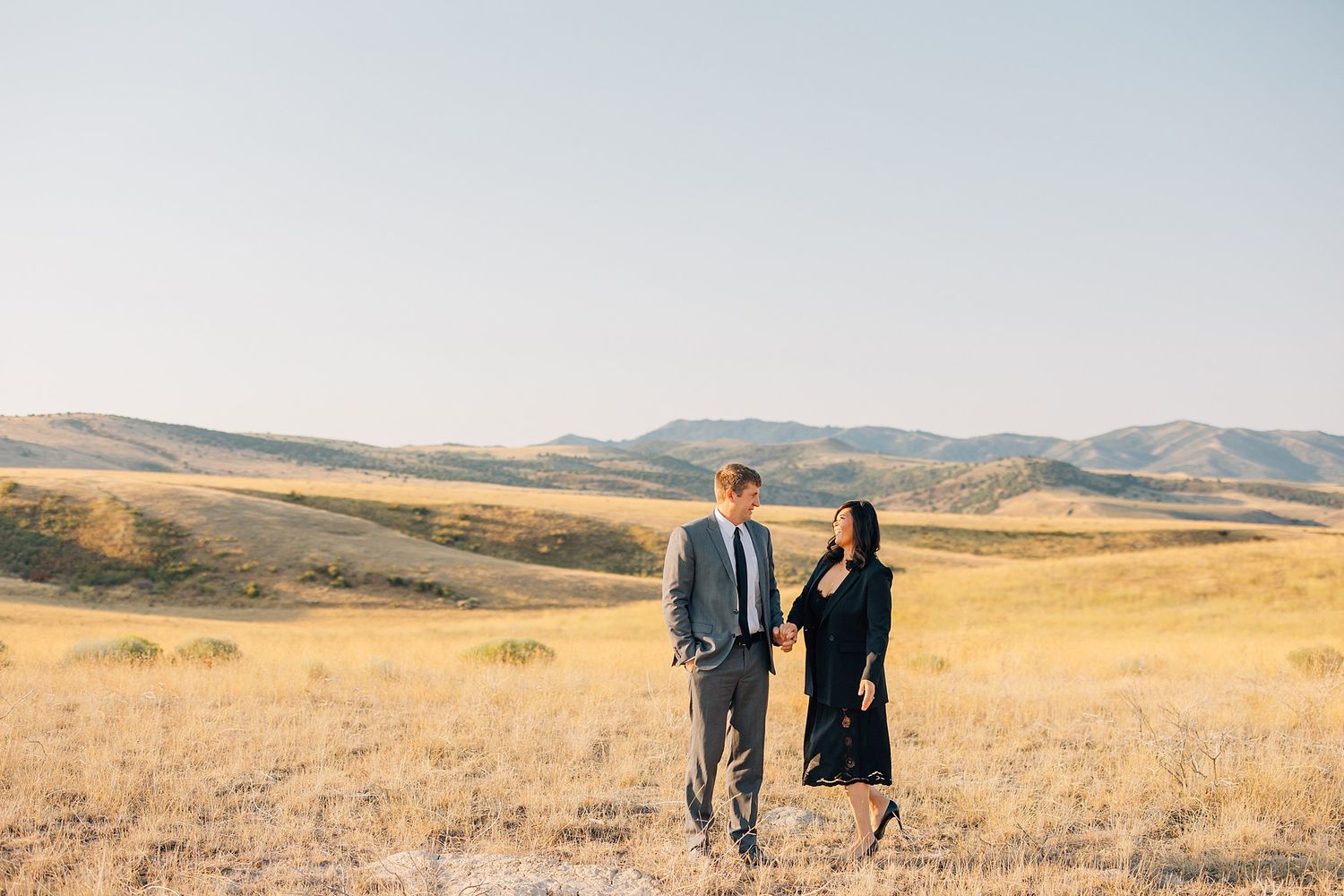 Two people walk together through golden rolling hills during sunset in a rural landscape.