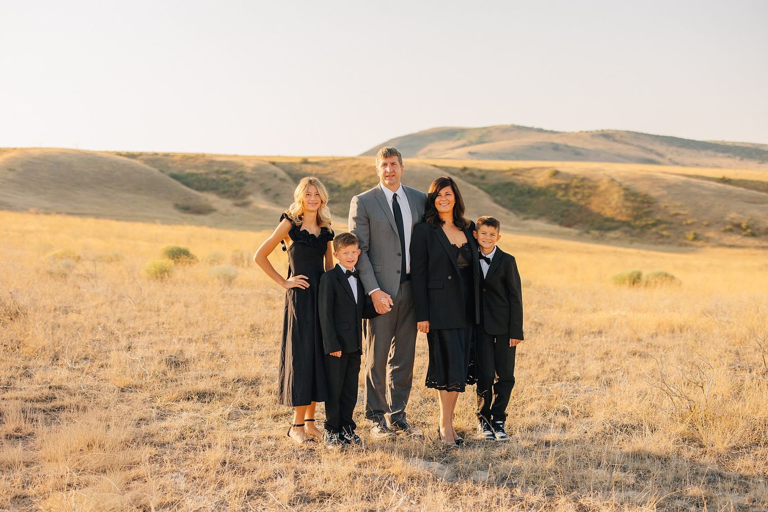 A group wearing formal attire poses together in a golden field at sunset for outdoor portraits.