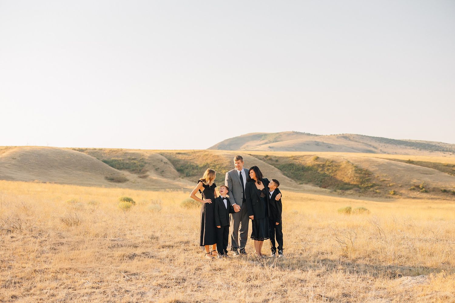Group of people walking together through golden autumn fields with rolling hills in the background at sunset.
