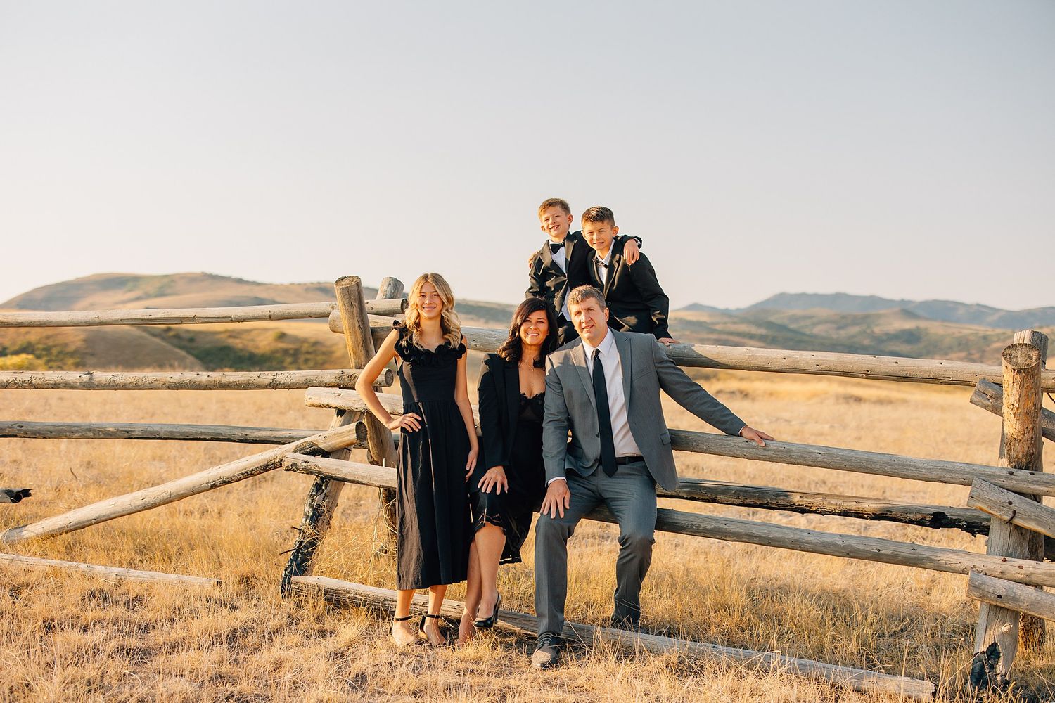 People gathered on wooden fence in rustic countryside setting with warm sunlit hills in the distance.