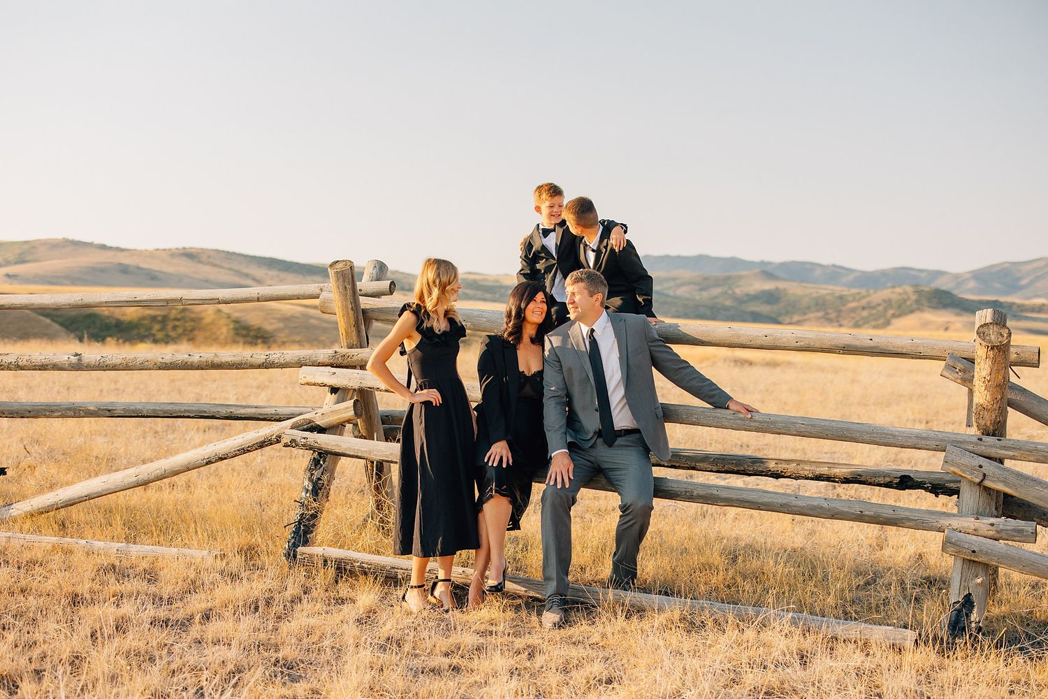 A group sits casually on a wooden fence against a backdrop of rolling hills during golden hour.