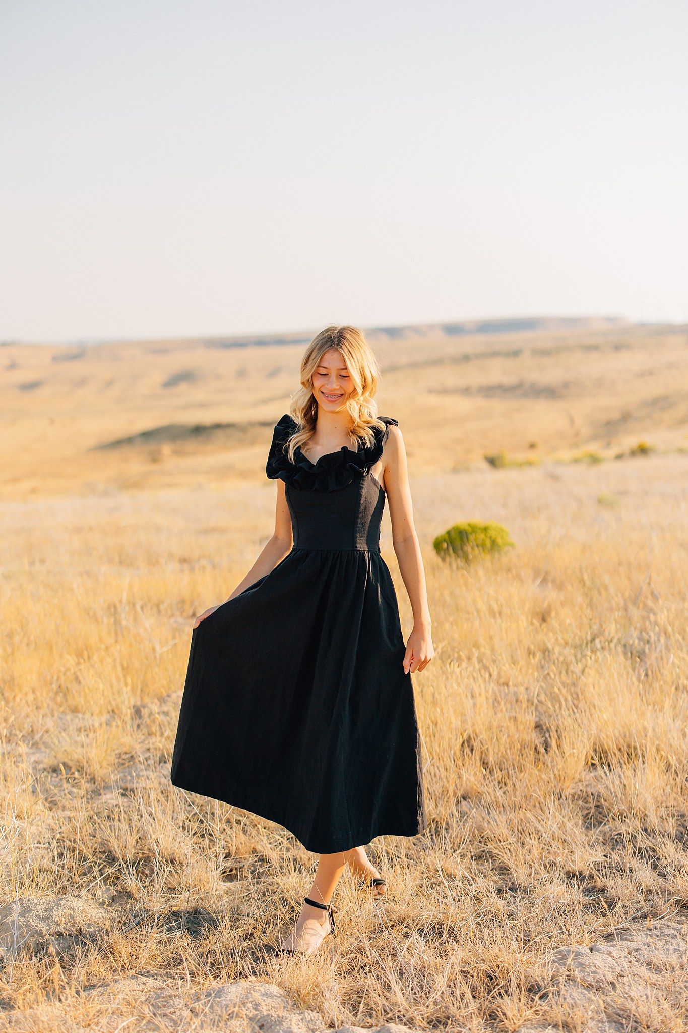 A person in a flowing black dress twirls gracefully in a golden sunlit field of dry grass.