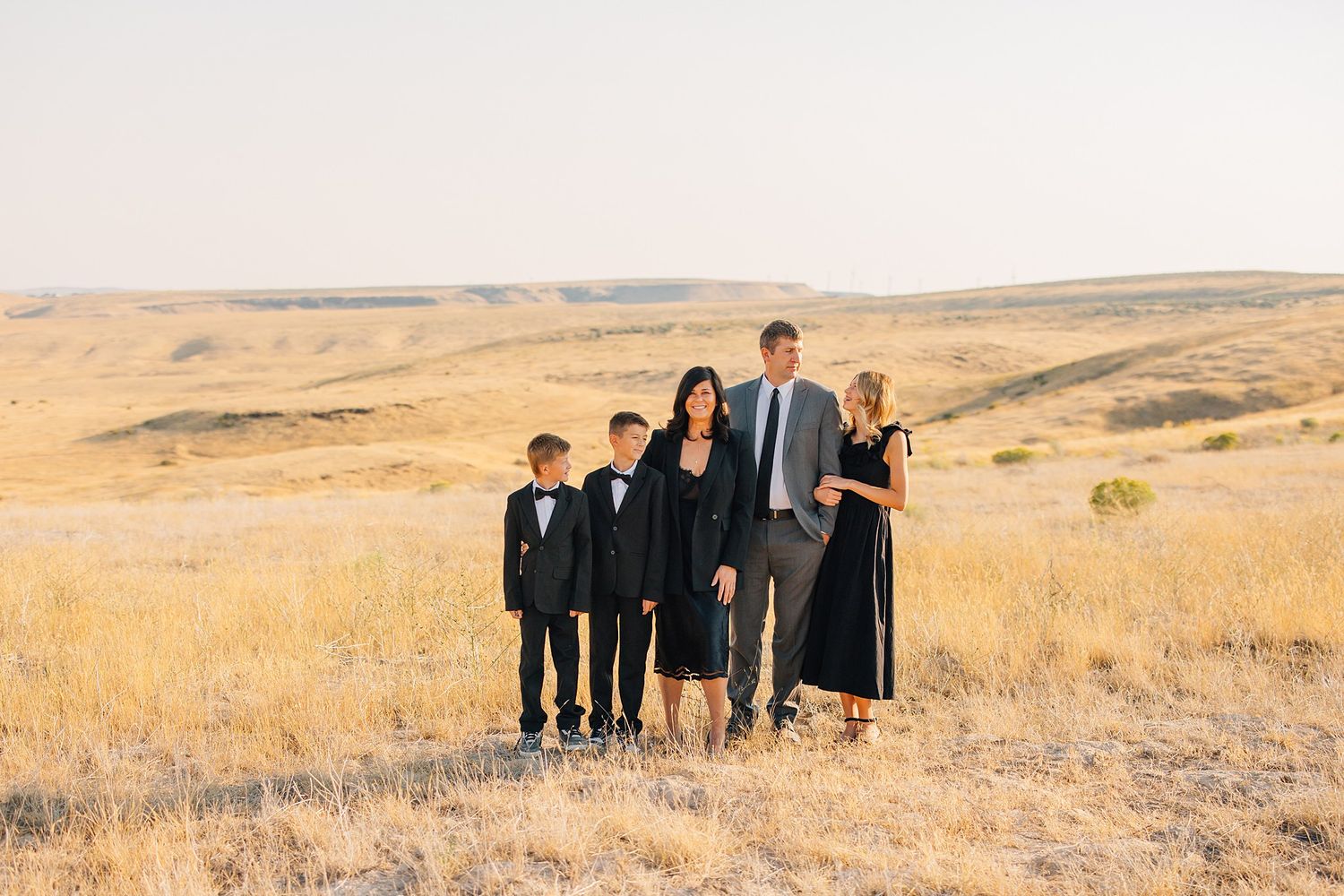 A group in formal attire stands together in a golden field during sunset.