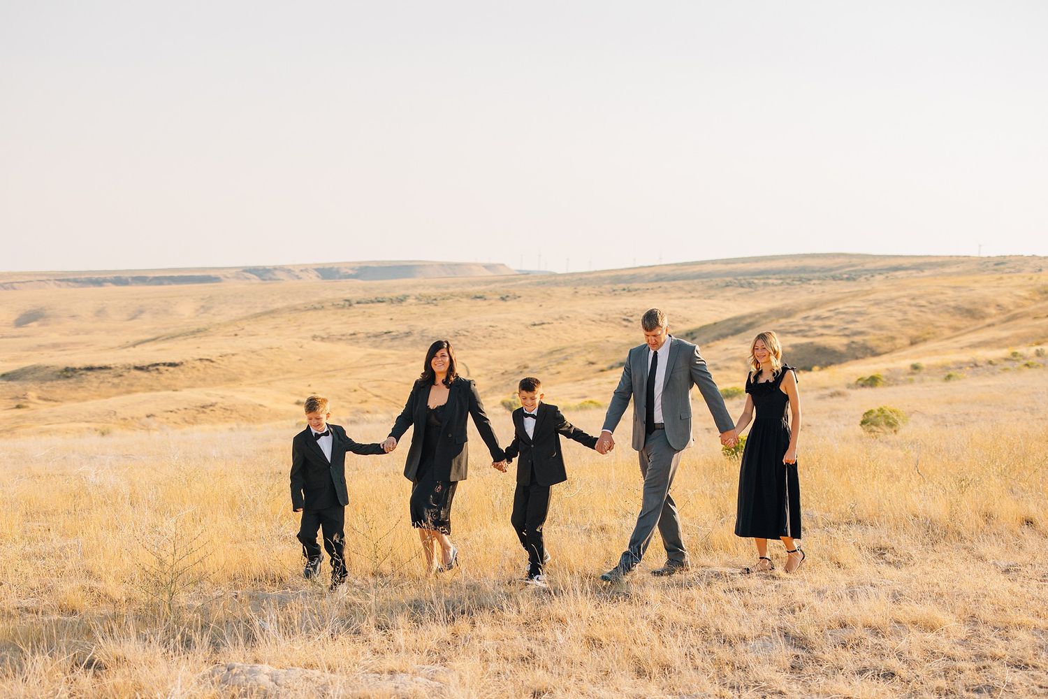 A group of people holding hands while walking through a golden autumn field at sunset.