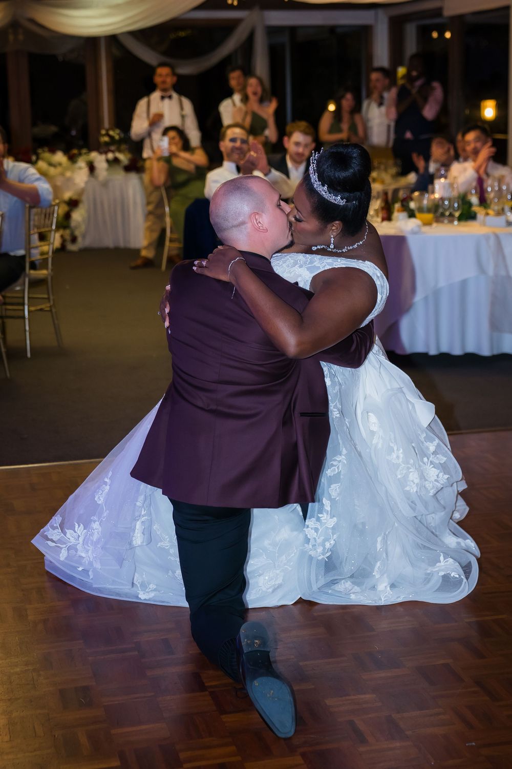 Newlyweds share their first dance at a wedding reception with guests and decorated tables in the background.