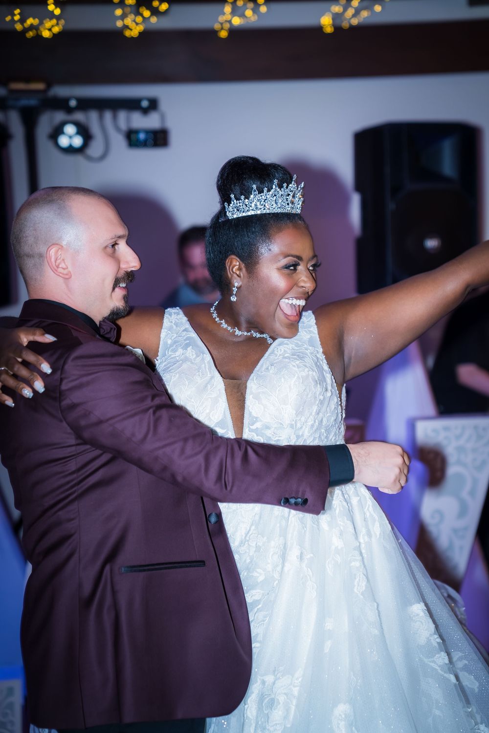 Wedding couple dances joyfully together in matching white gown and brown suit during their reception celebration.