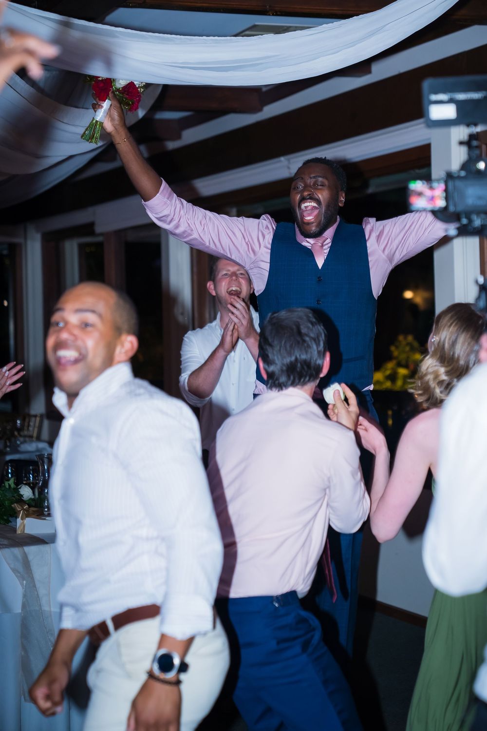Wedding guests dance and celebrate joyfully on the dance floor at an indoor reception venue.