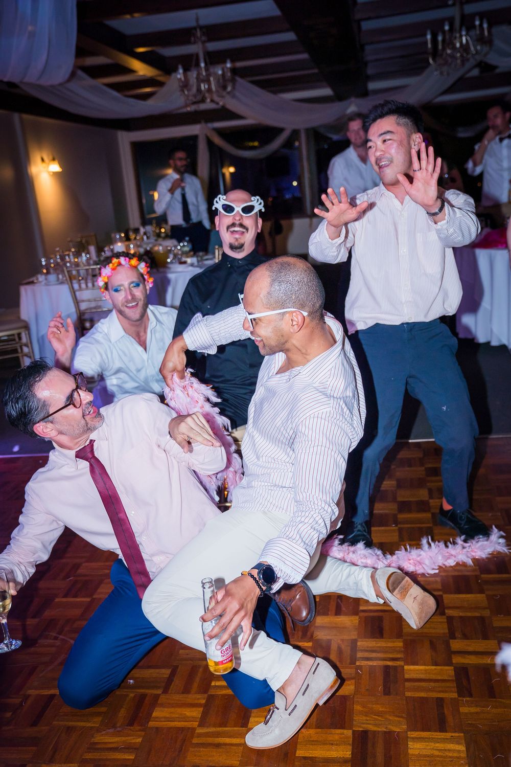 Wedding guests dance energetically on a wooden dance floor during a reception celebration.