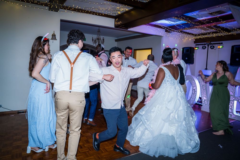Wedding guests dance together on the dance floor during a reception celebration with festive lighting.