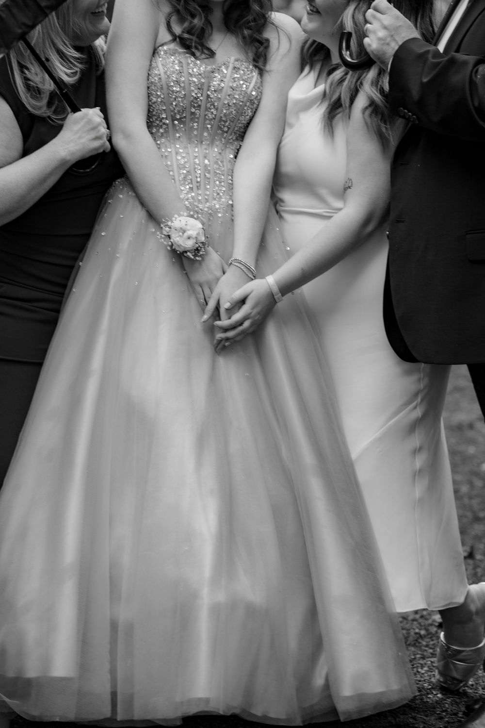 Black and white photo of women in elegant formal gowns holding hands at a prom or wedding event.