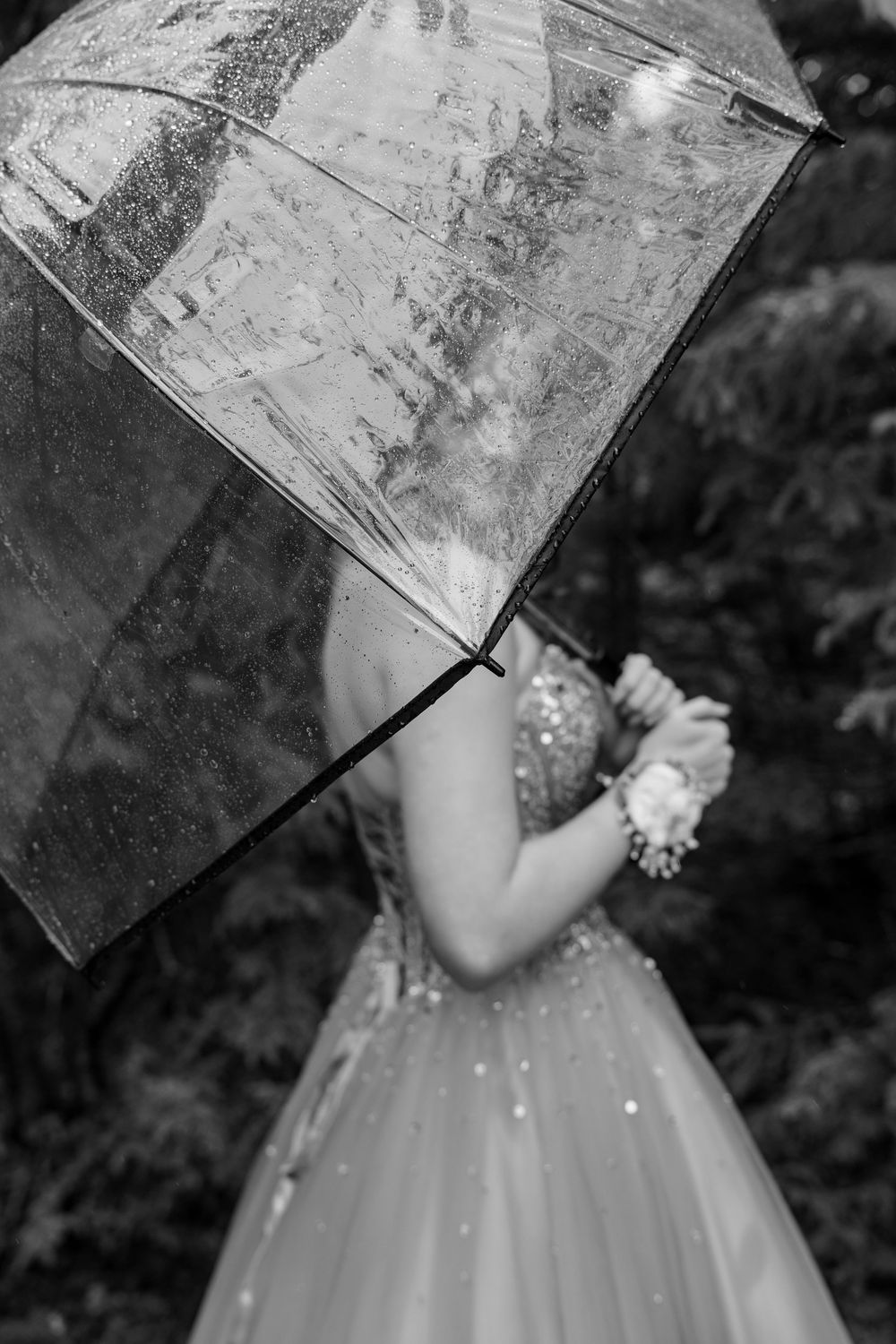Black and white photo of a woman in a sequined gown holding a clear umbrella in the rain.