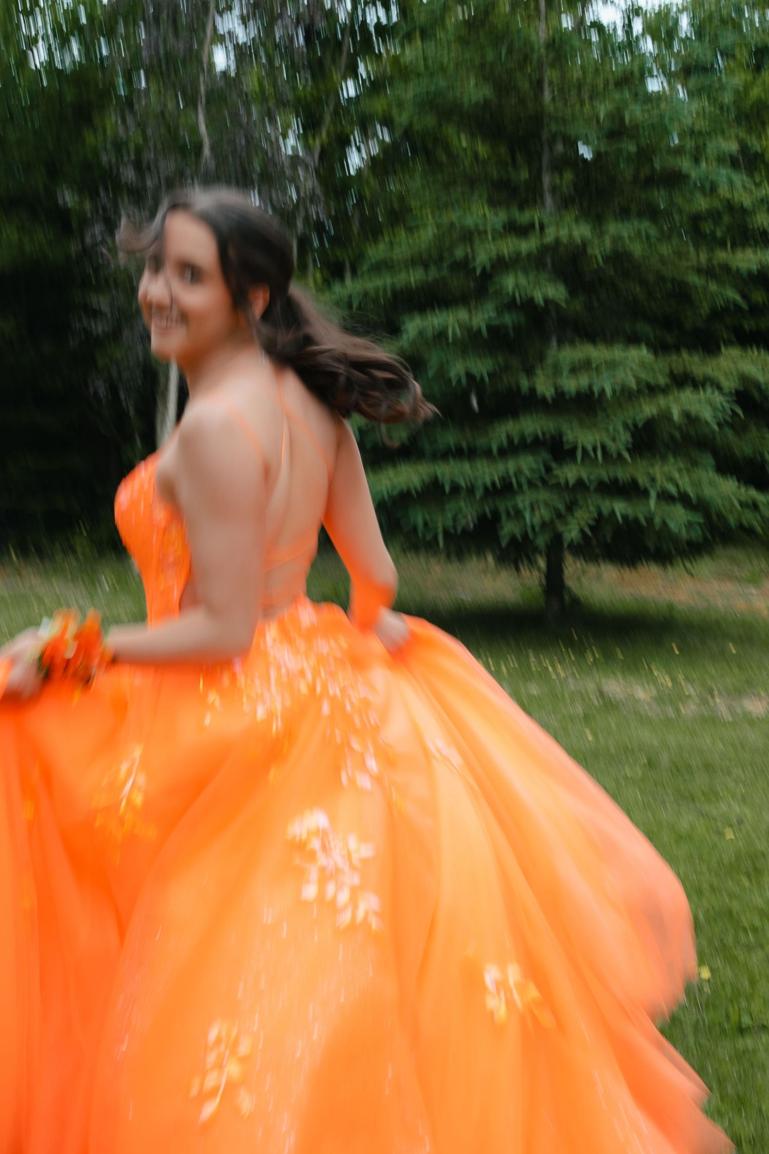 A person in a flowing bright orange dress spins gracefully in a garden setting, creating a circular motion effect.