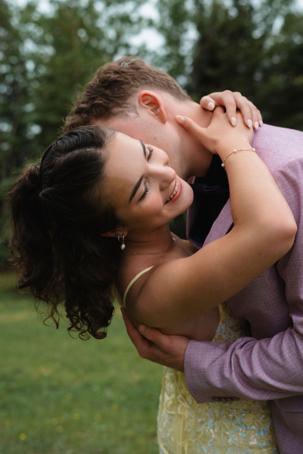 A couple shares a romantic embrace outdoors, with the woman smiling joyfully as the man kisses her cheek.
