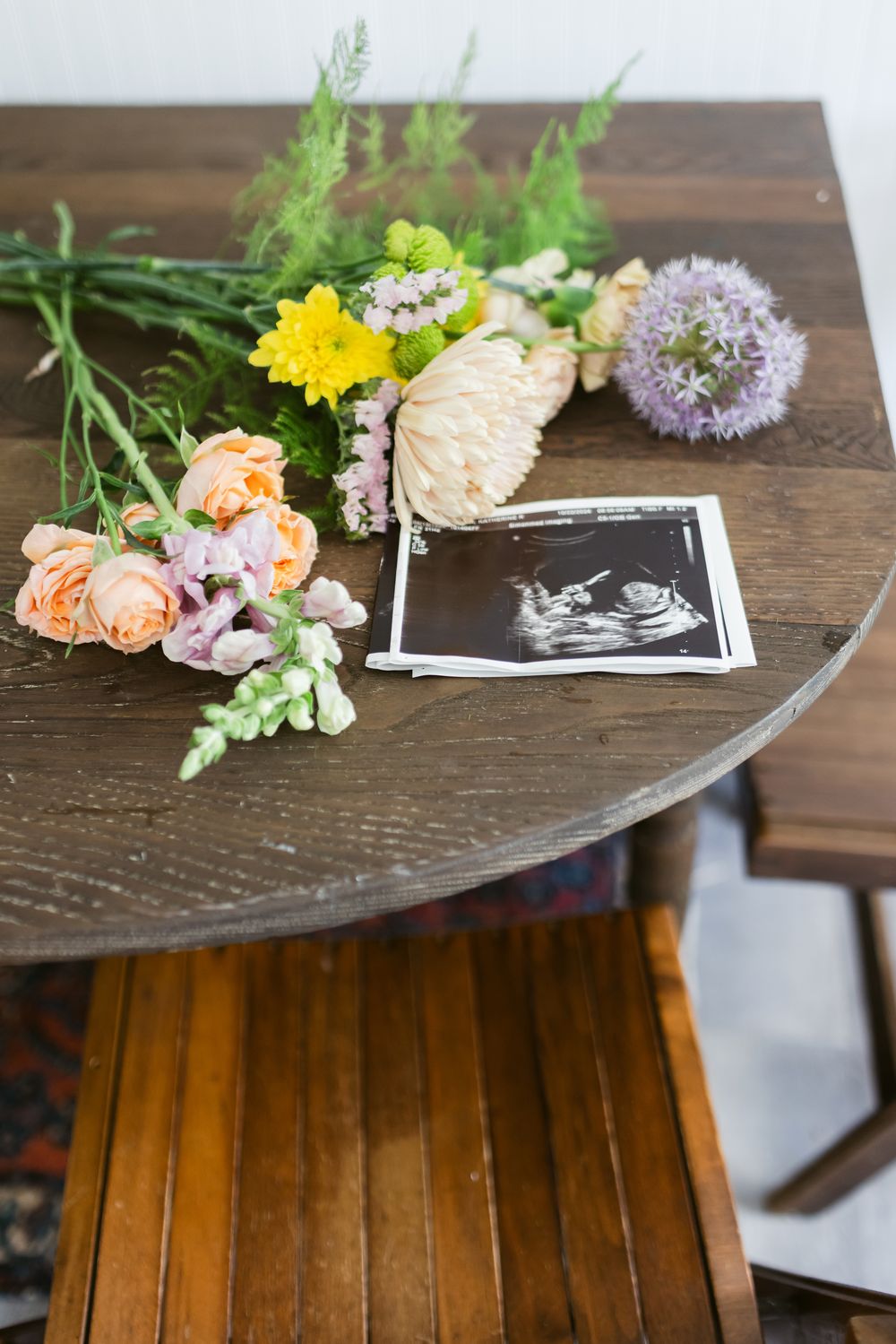 A baby ultrasound lays next to flowers places on a wooden table at a newborn shoot in Berwick, Maine. Southern Maine newborn photographer.