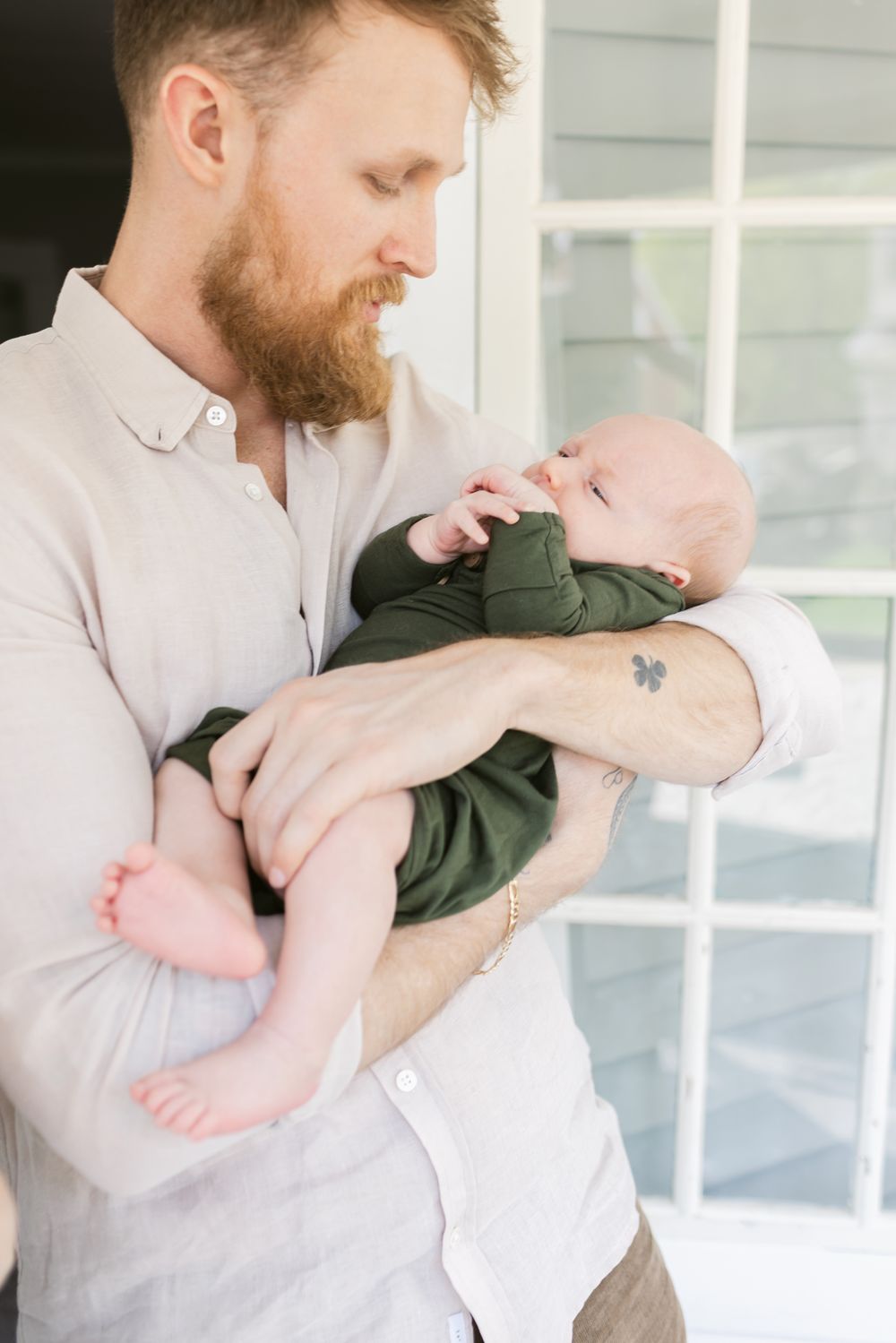 A father gazes at his newborn son wearing forest green on their porch for newborn photos in the Seacoast region of NH. Concord newborn.