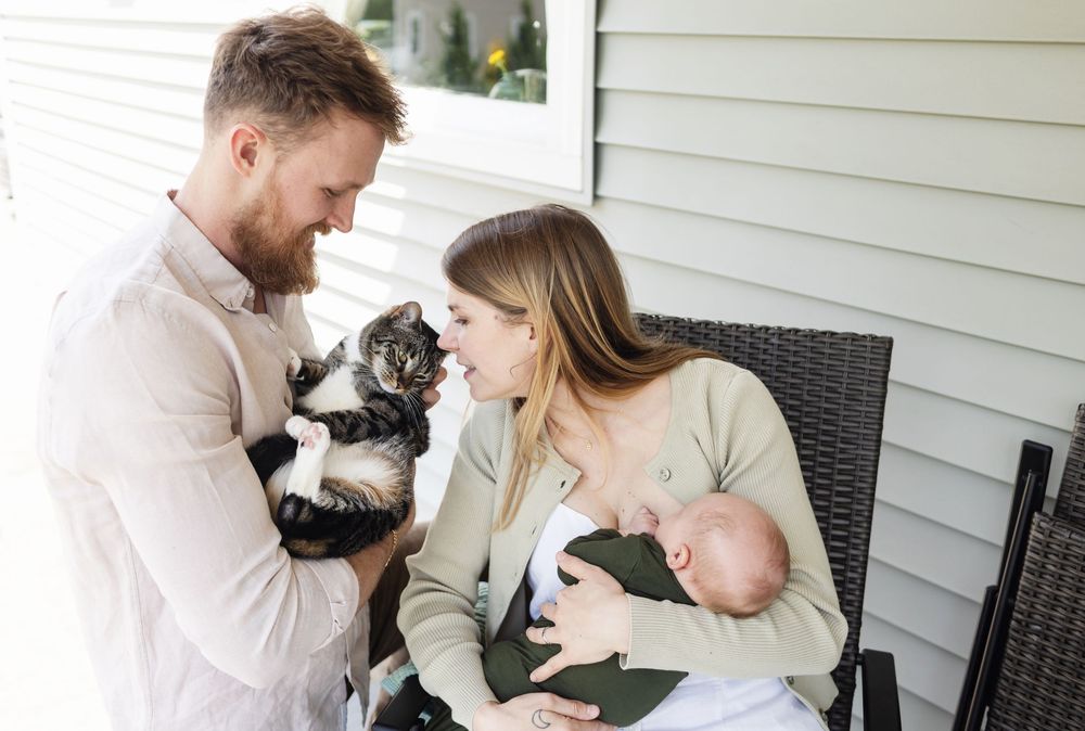 A mother kisses her cat being held by her husband on its head while holding her newborn son on their porch for newborn photos in Berwick.