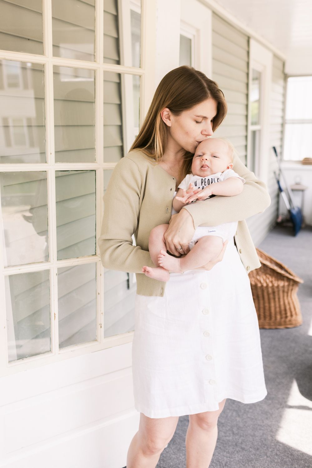 A mother wearing a mint sweater kisses her newborn son on the forehead on her porch for newborn home photos in the Seacoast region of NH.