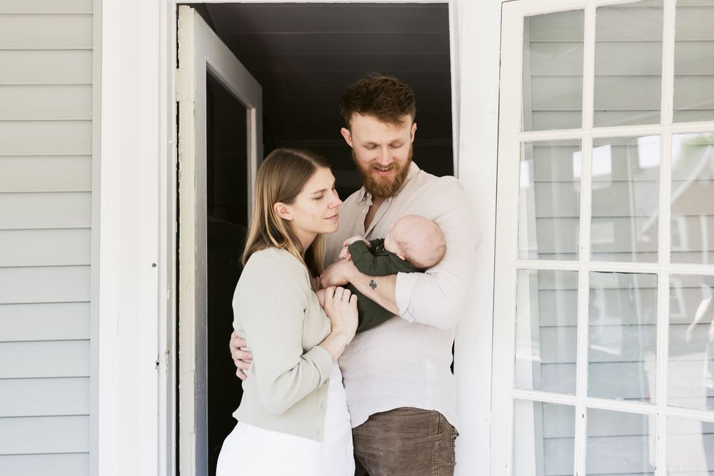A couple gazes at their newborn son in the doorway of their porch for a lifestyle newborn photo shoot. Concord, Manchester newborn photos
