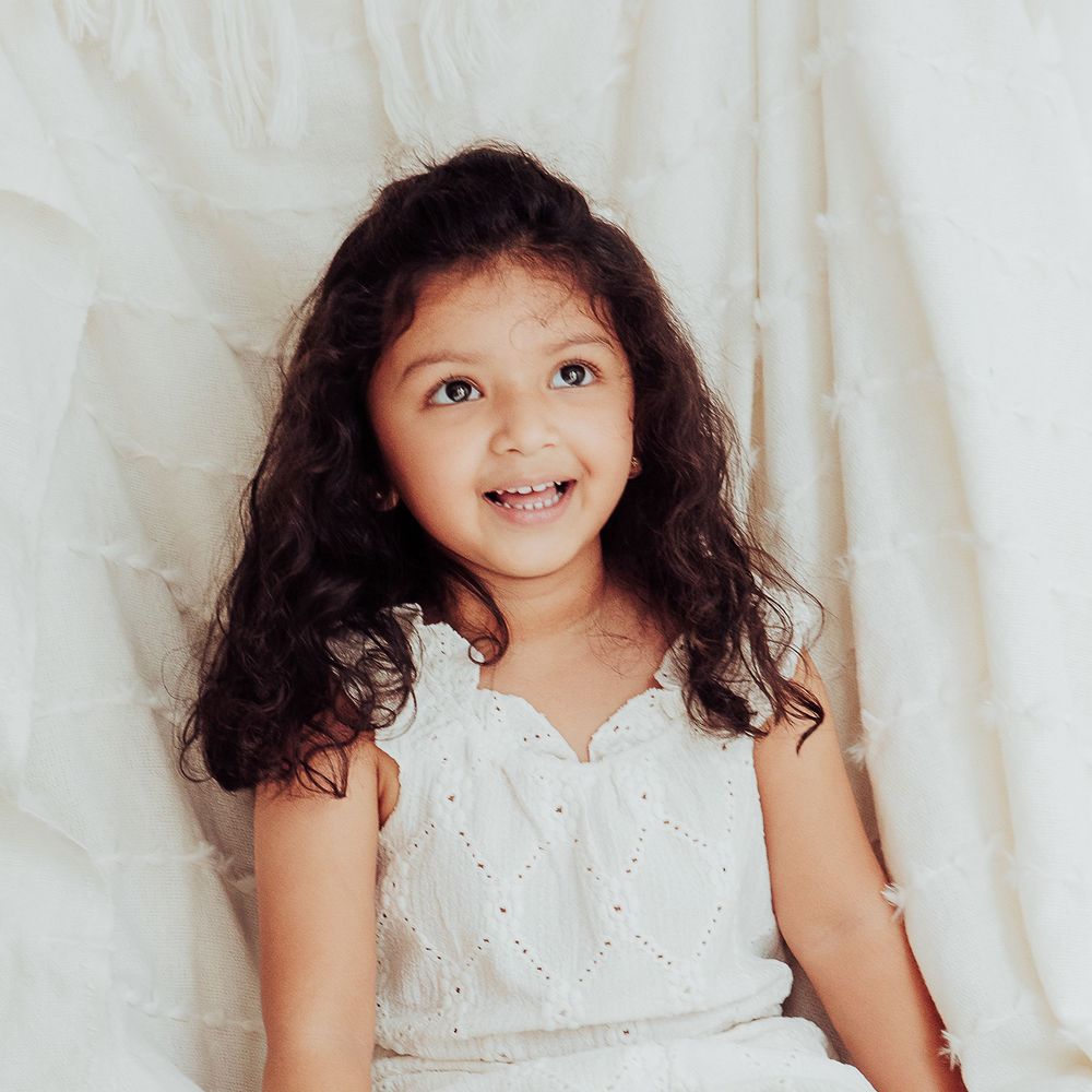 Young girl laughing sitting on a cream blanked in a studio setting.