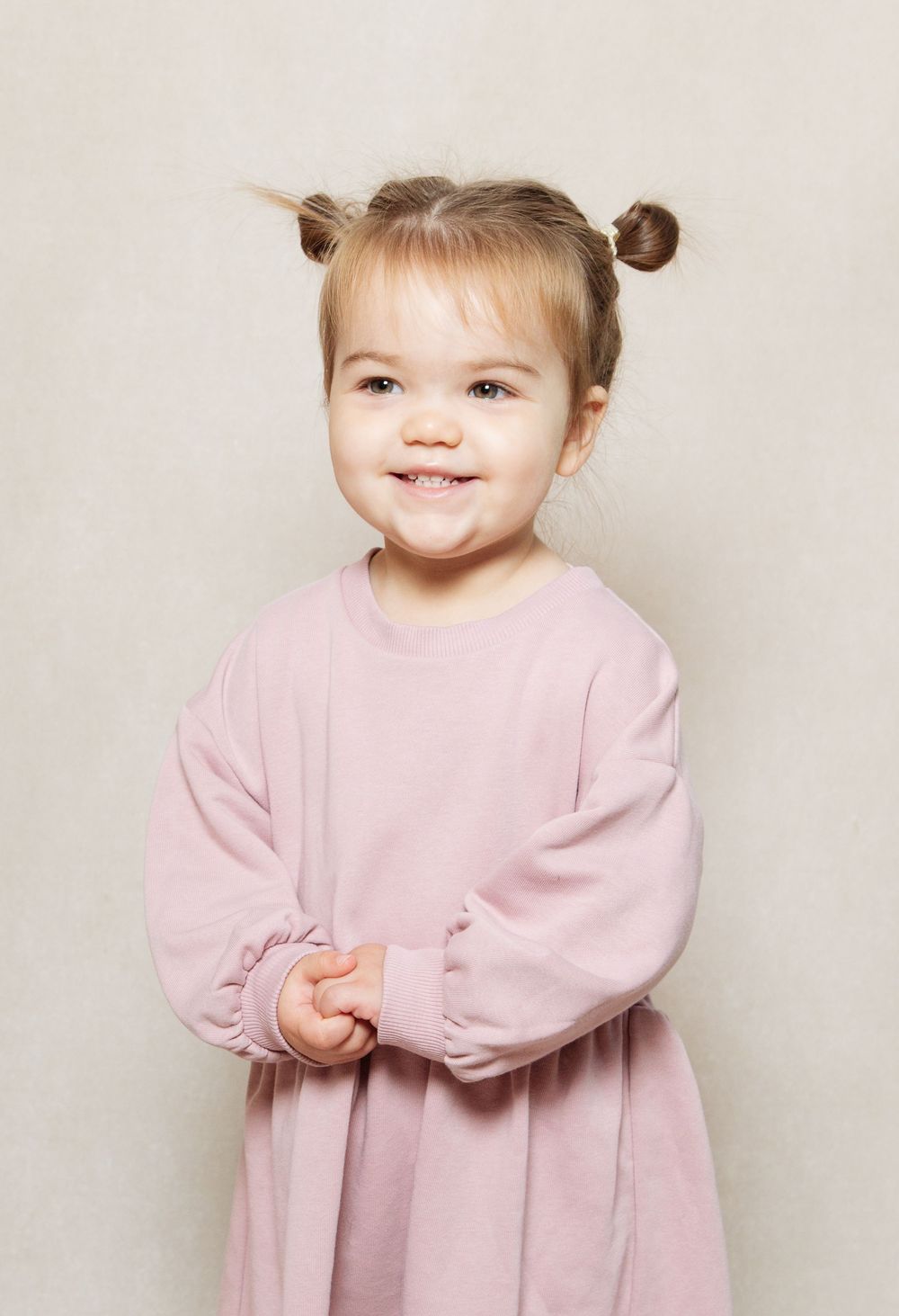 Cream studio setting of a little girl smiling cheekily at the camera.
