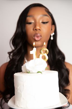 A white birthday cake with lit number 18 candles glows warmly against a soft blurred background.