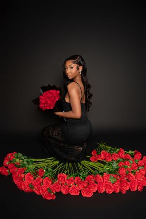 A figure in a black dress poses elegantly with vibrant red roses against a dark background in a dramatic photo series.