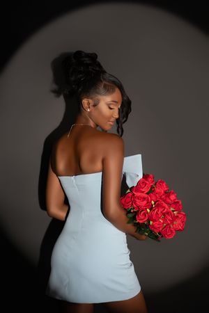 A figure in a white dress holds vibrant red roses against a dark background in an artistic portrait series.