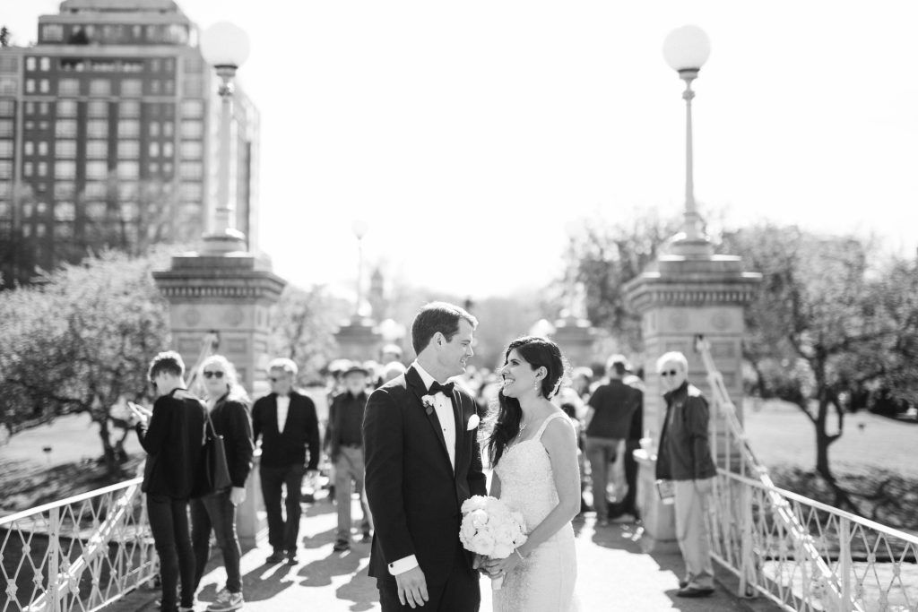 Black and white wedding portrait on bridge with city skyline in background.