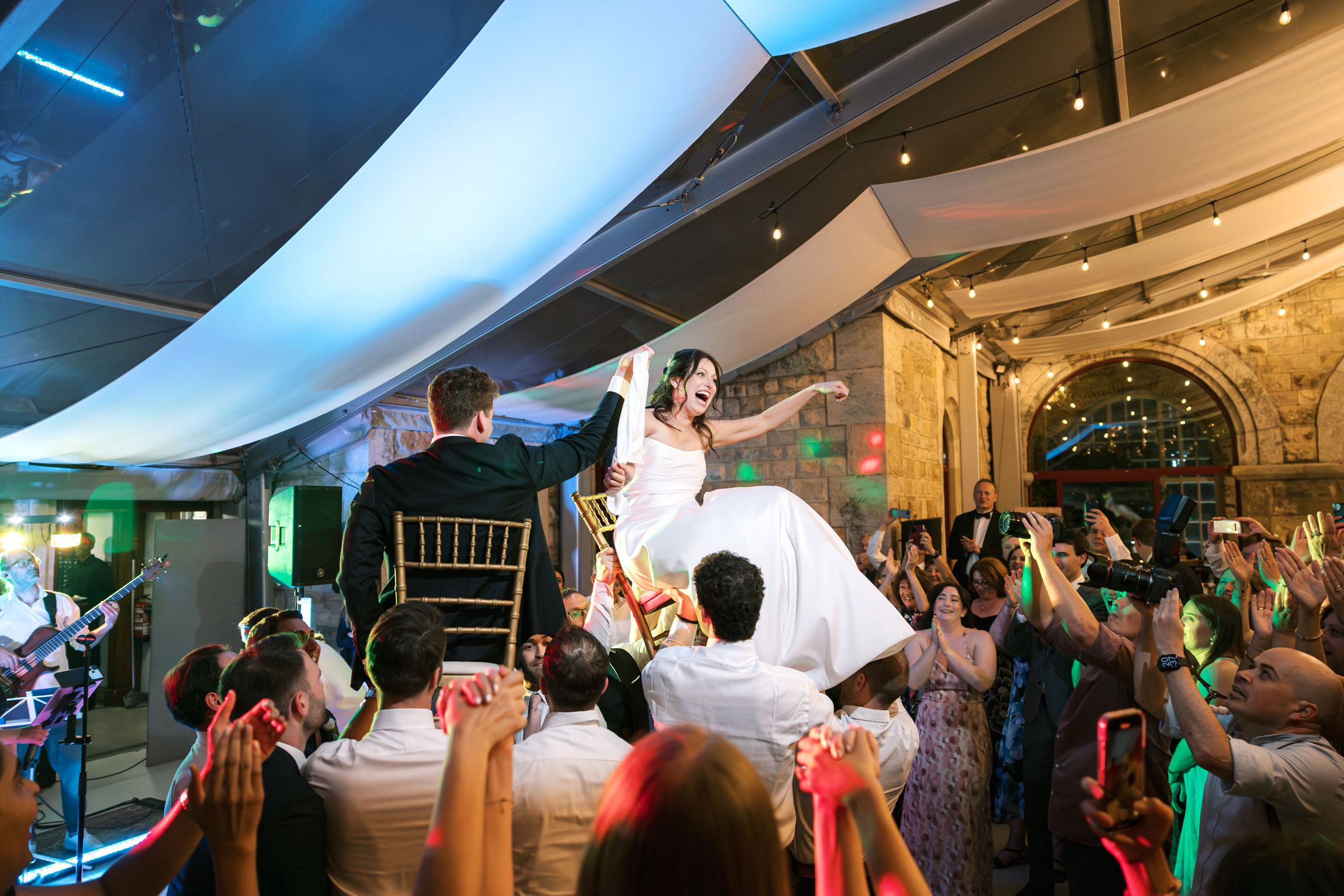 Jewish wedding hora dance with bride and groom lifted on chairs at Forte da Cruz in Cascais Portugal