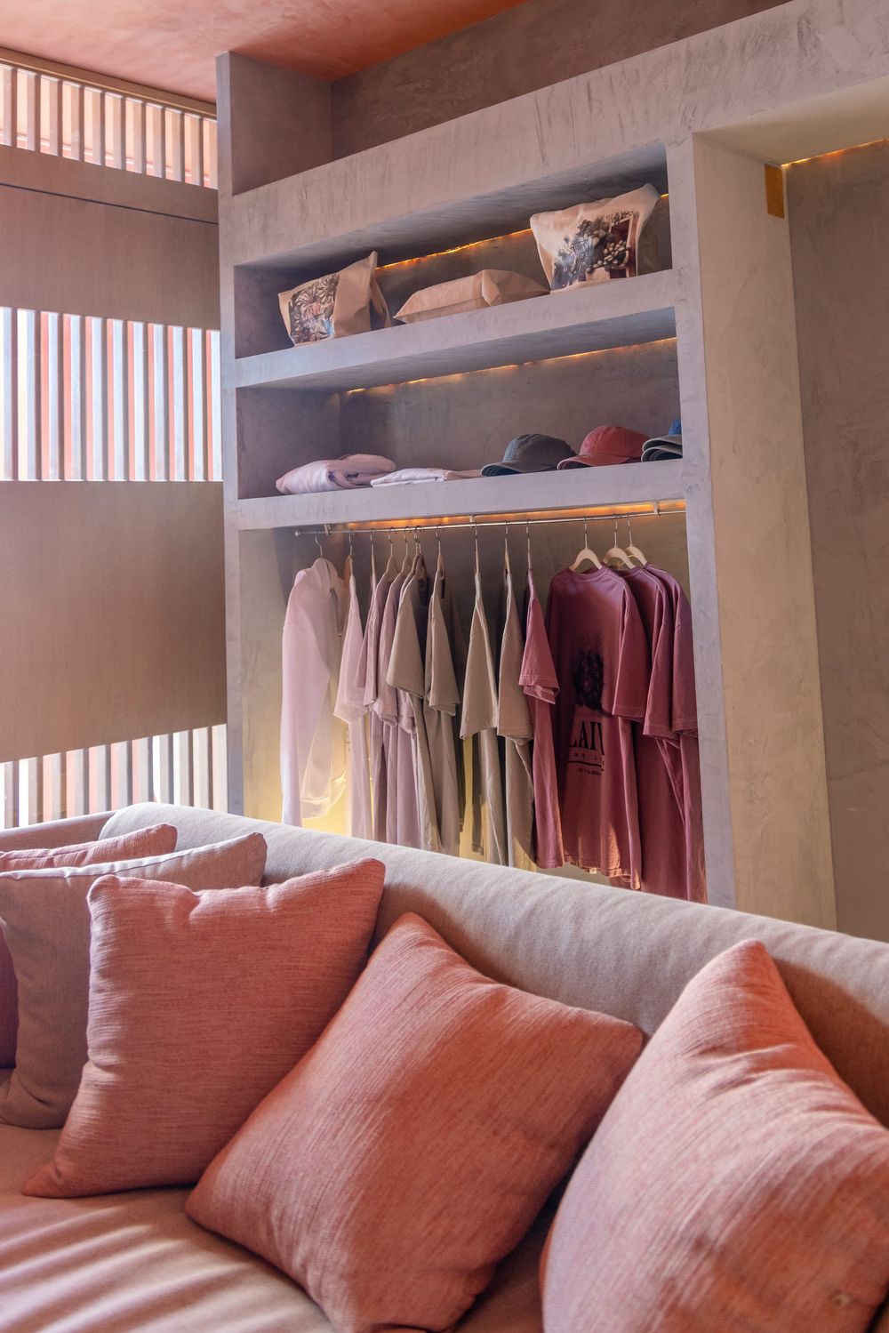 Elegant walk-in closet with pink and mauve robes on hangers, built-in shelves, and a cozy sofa with blush pillows.